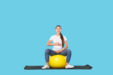 Beautiful pregnant woman doing exercises on fitball against light blue background