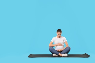 Photo of Beautiful pregnant woman on exercise mat against light blue background, space for text