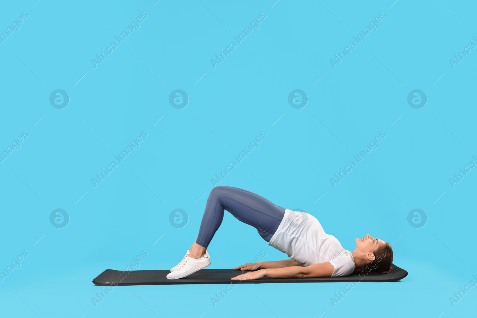 Photo of Beautiful pregnant woman doing stretching exercises on mat against light blue background