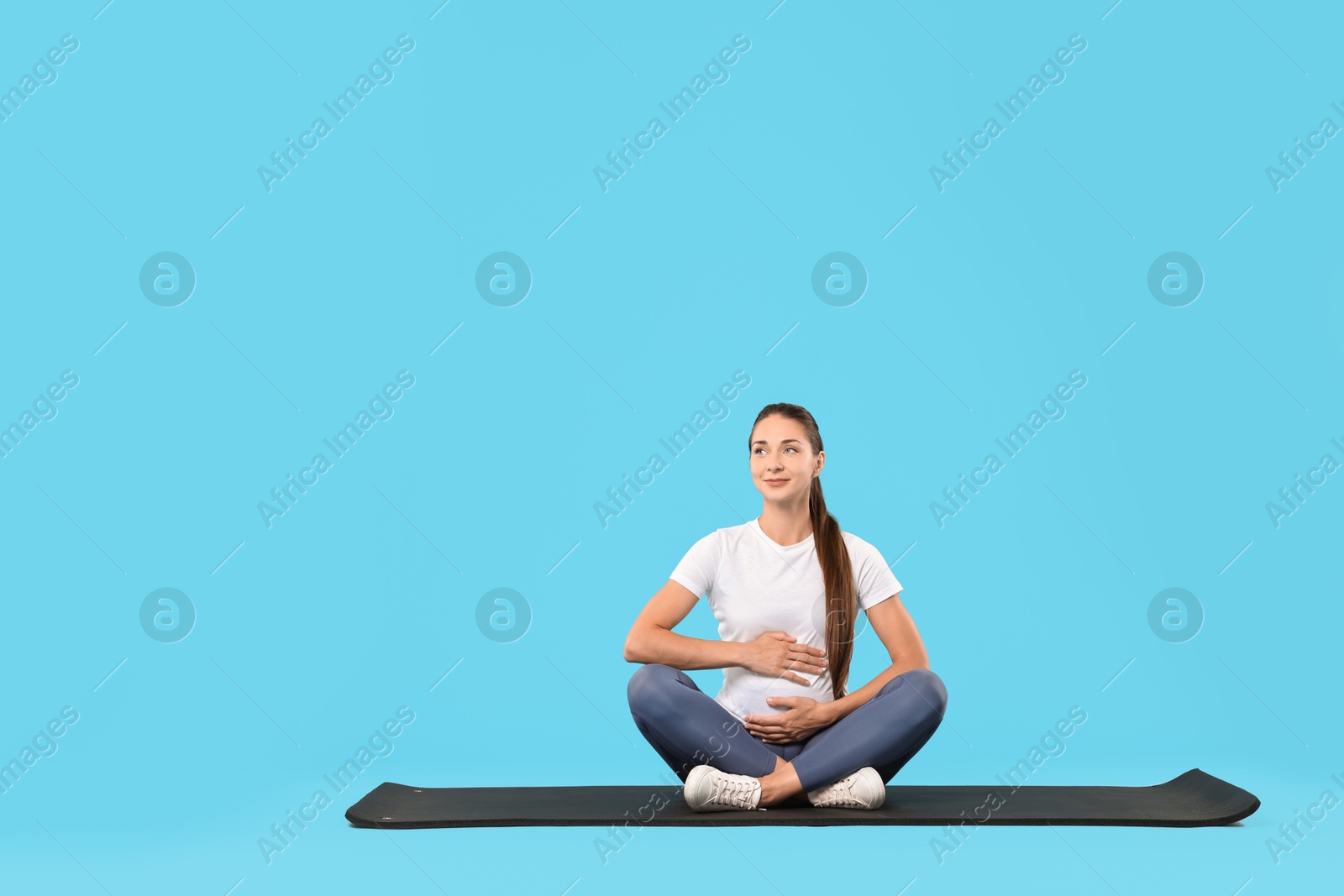 Photo of Beautiful pregnant woman on exercise mat against light blue background, space for text