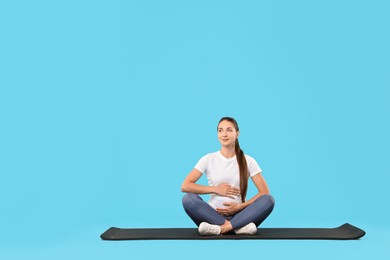Photo of Beautiful pregnant woman on exercise mat against light blue background, space for text