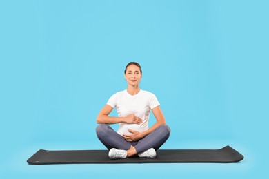 Photo of Beautiful pregnant woman on exercise mat against light blue background