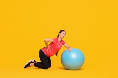 Beautiful pregnant woman doing exercises with fitball on yellow background