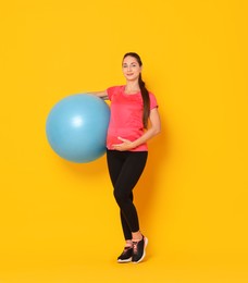 Photo of Beautiful pregnant woman with fitball on yellow background