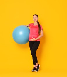 Beautiful pregnant woman with fitball on yellow background