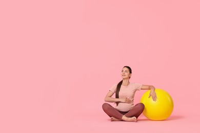 Beautiful pregnant woman with fitball on pink background, space for text