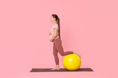 Photo of Beautiful pregnant woman with fitball doing exercises on mat against pink background