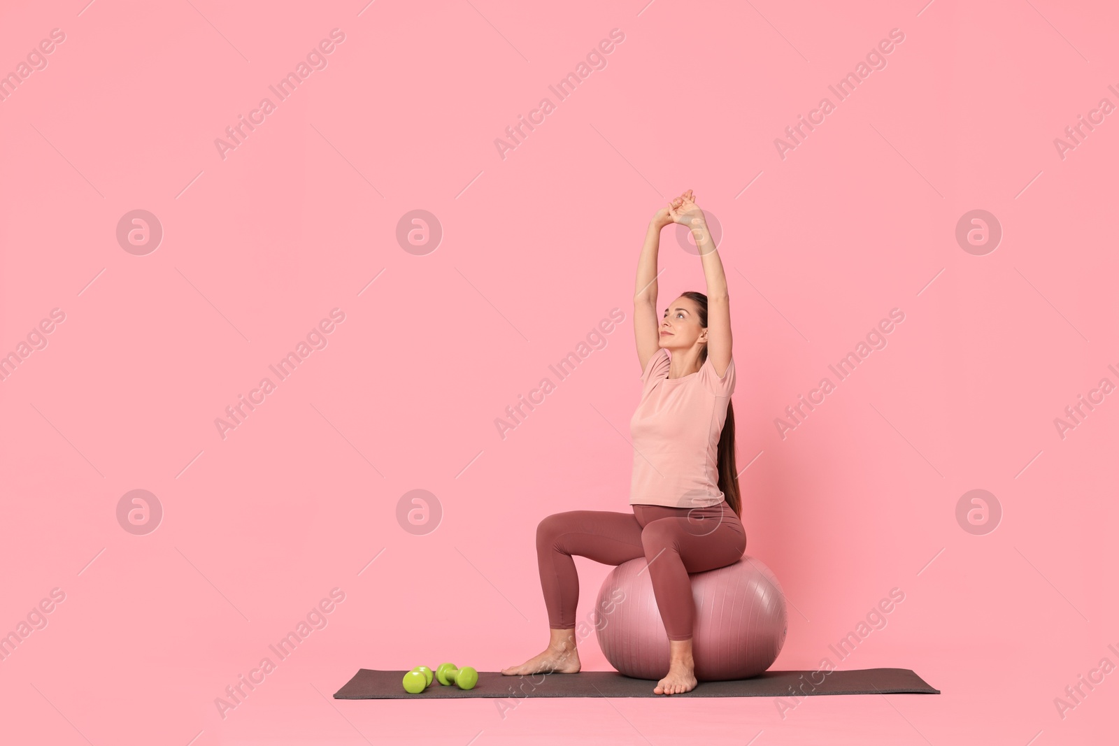 Photo of Beautiful pregnant woman doing exercises on fitball against pink background