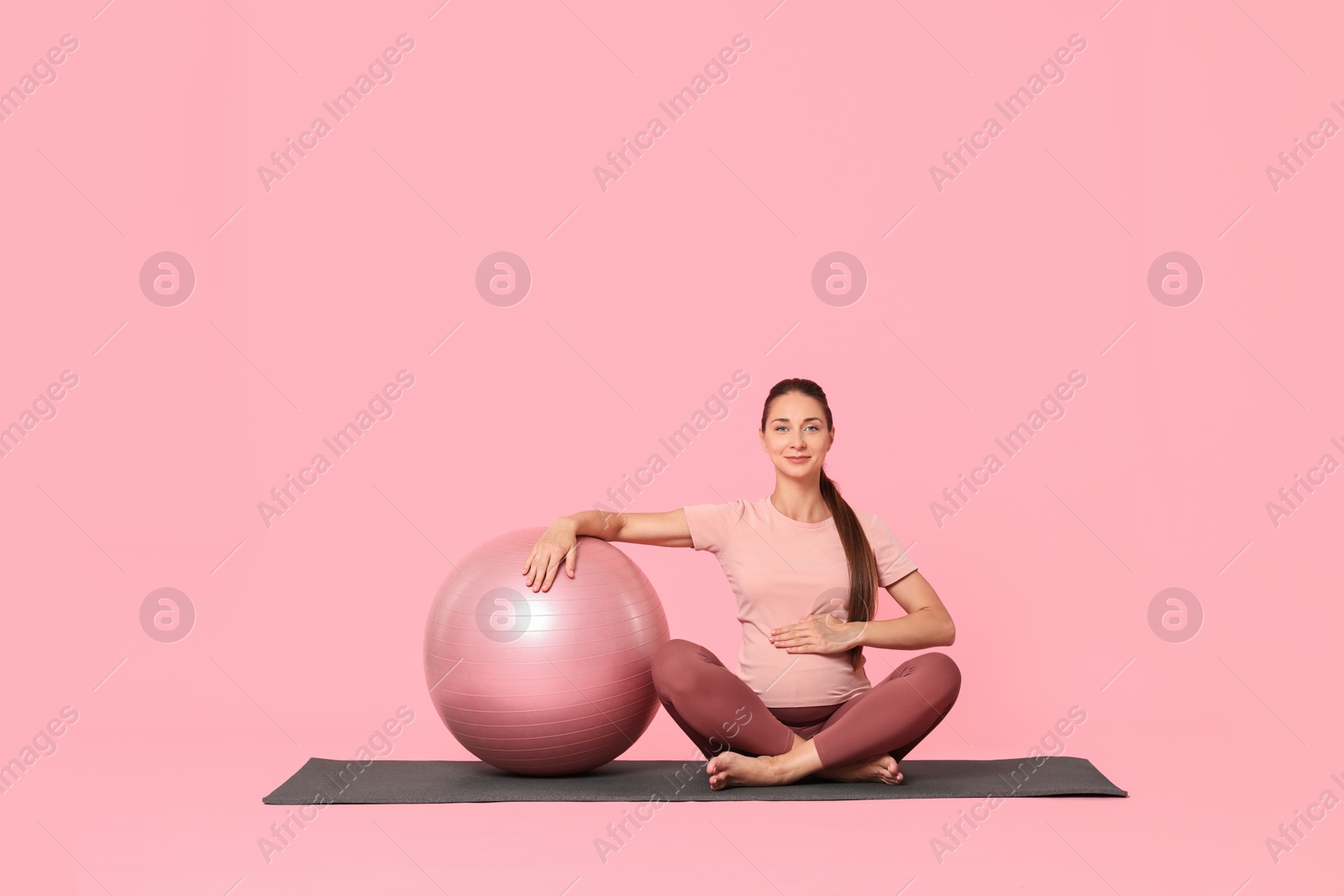 Photo of Beautiful pregnant woman with fitball on exercise mat against pink background