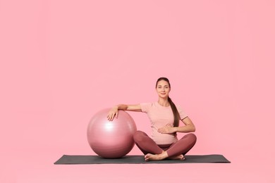 Photo of Beautiful pregnant woman with fitball on exercise mat against pink background