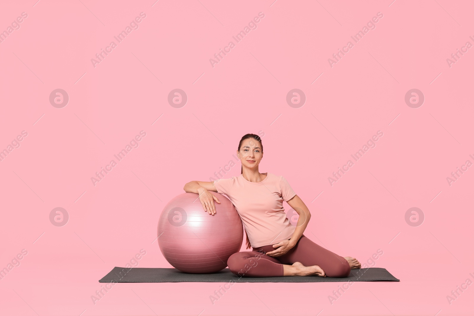 Photo of Beautiful pregnant woman with fitball on exercise mat against pink background