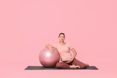 Beautiful pregnant woman with fitball on exercise mat against pink background