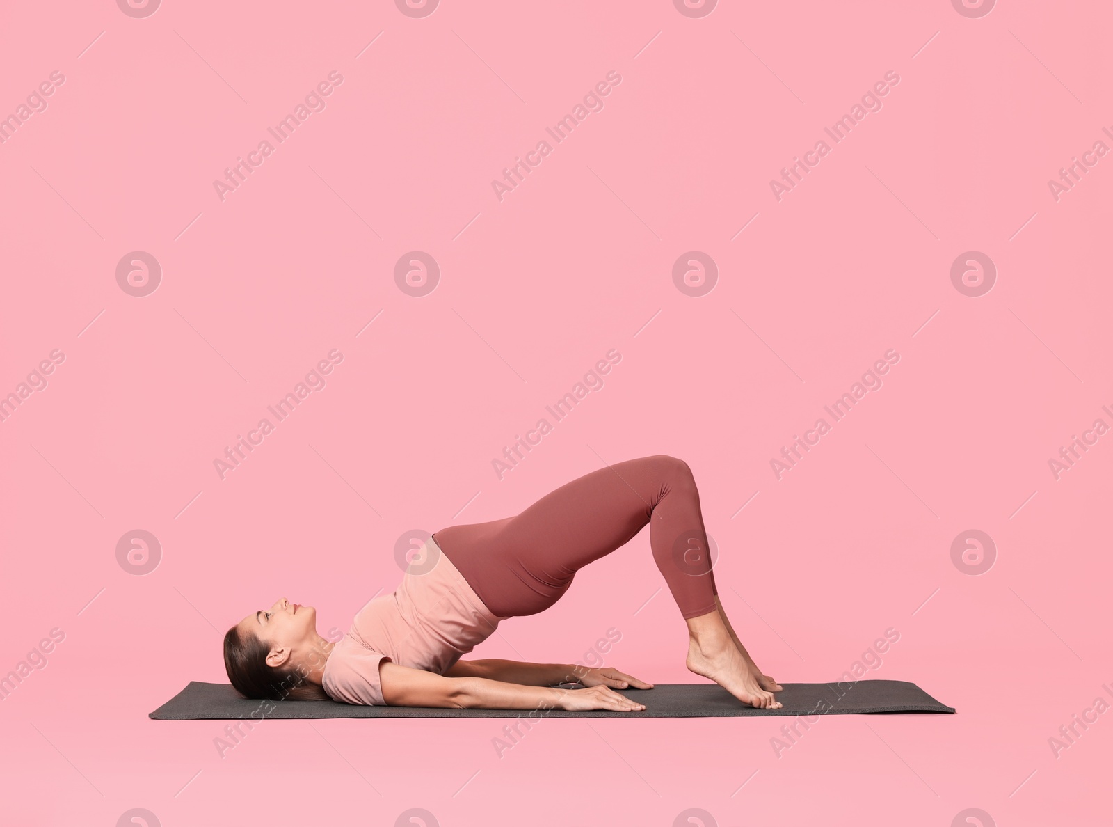 Photo of Beautiful pregnant woman doing stretching exercises on mat against pink background