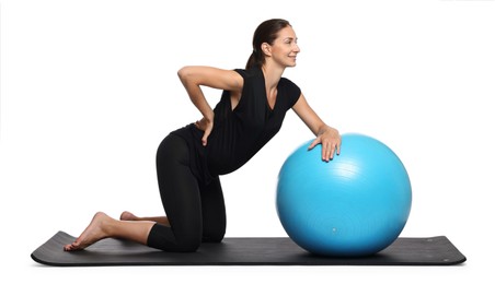 Beautiful pregnant woman with fitball doing exercises on mat against white background