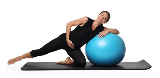 Beautiful pregnant woman with fitball doing exercises on mat against white background