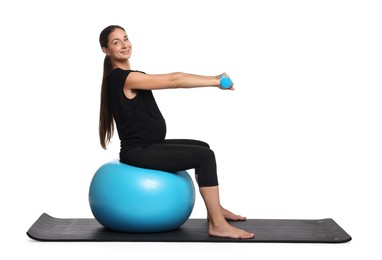 Beautiful pregnant woman with dumbbells doing exercises on fitball against white background