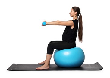 Beautiful pregnant woman with dumbbells doing exercises on fitball against white background