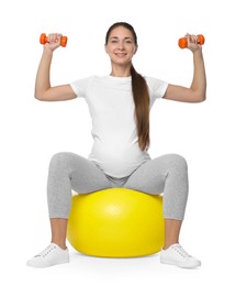 Beautiful pregnant woman with dumbbells doing exercises on fitball against white background