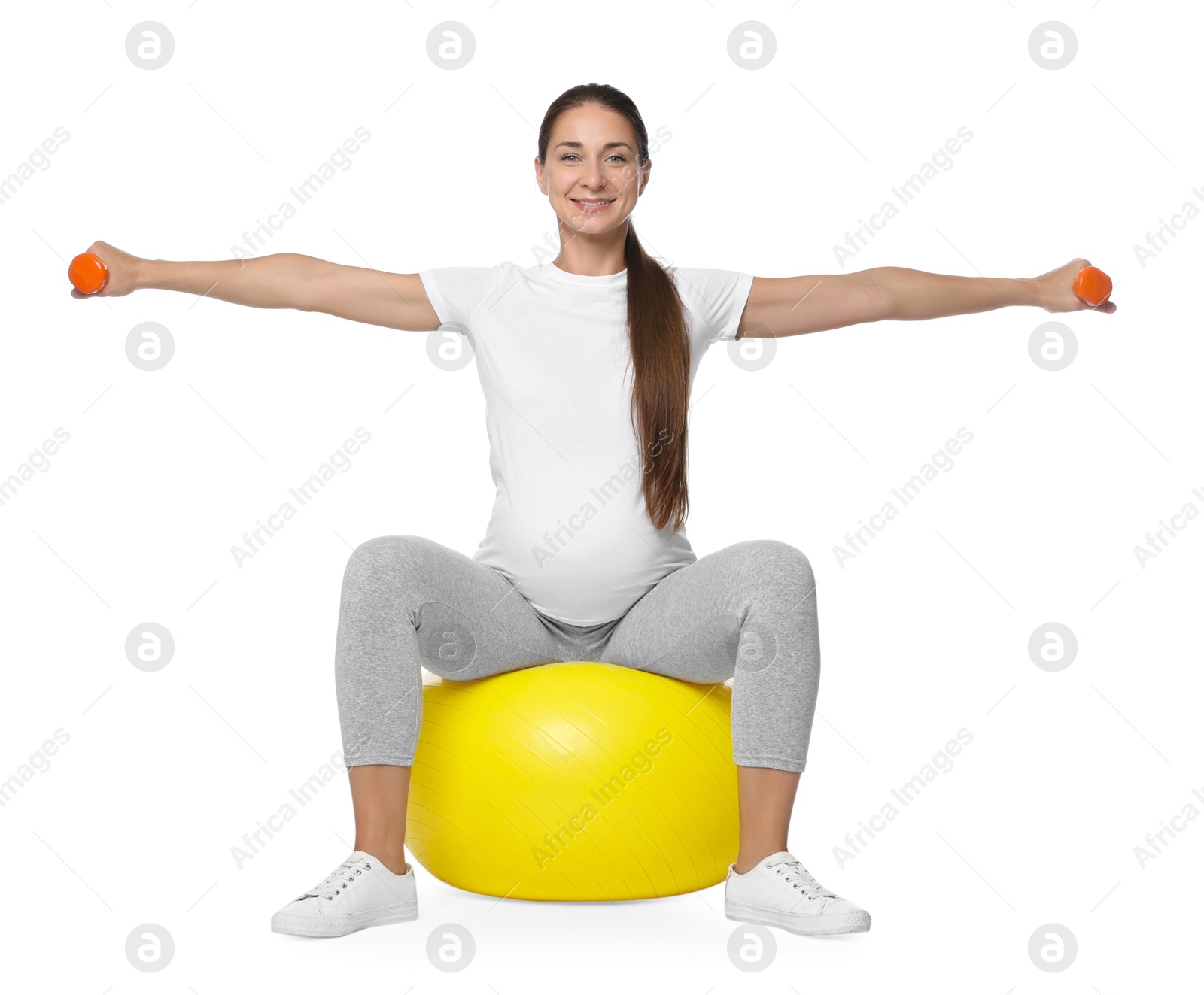 Photo of Beautiful pregnant woman with dumbbells doing exercises on fitball against white background