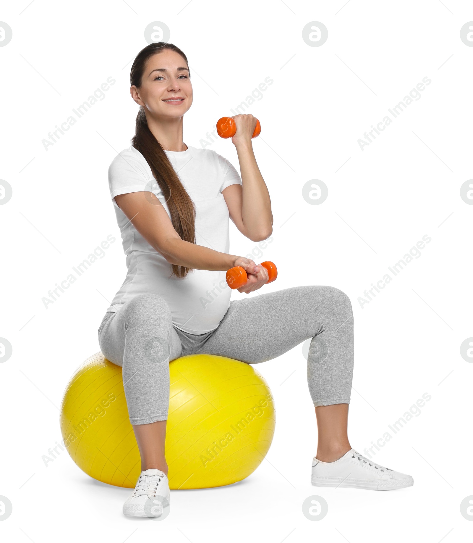 Photo of Beautiful pregnant woman with dumbbells doing exercises on fitball against white background