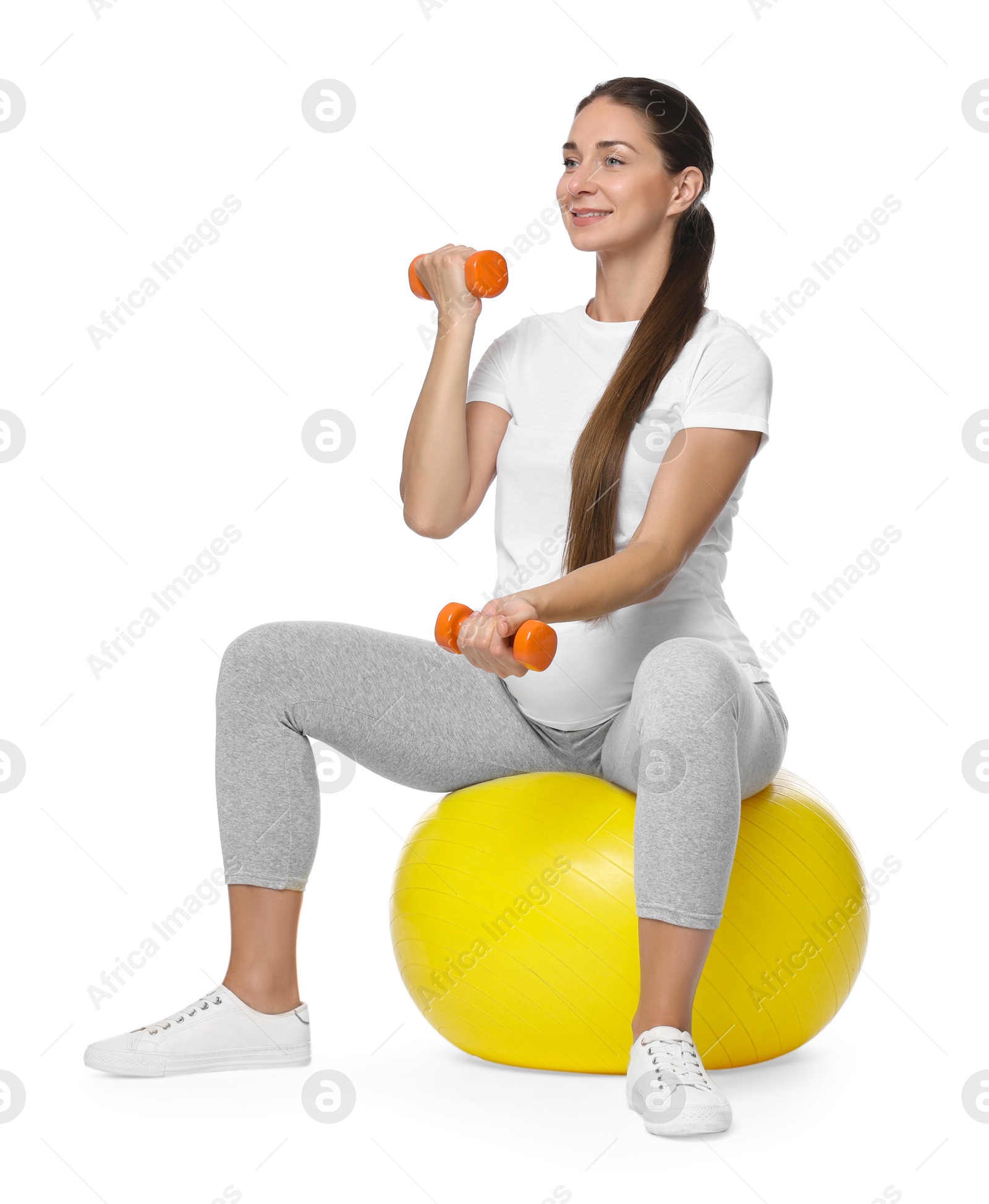 Photo of Beautiful pregnant woman with dumbbells doing exercises on fitball against white background