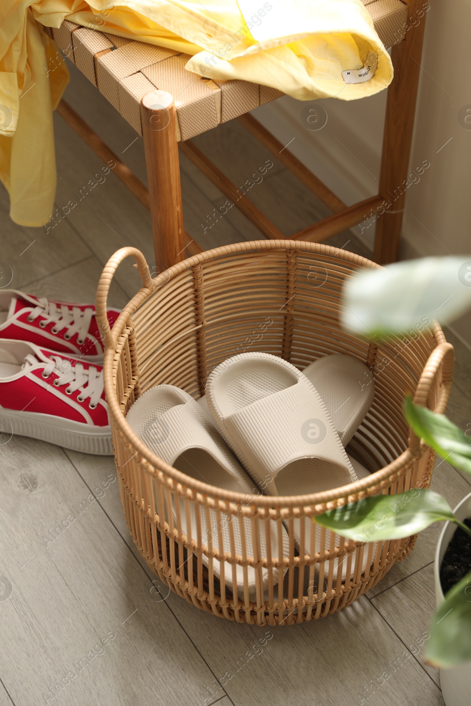 Photo of Basket with slippers for guests and sneakers in entryway at home