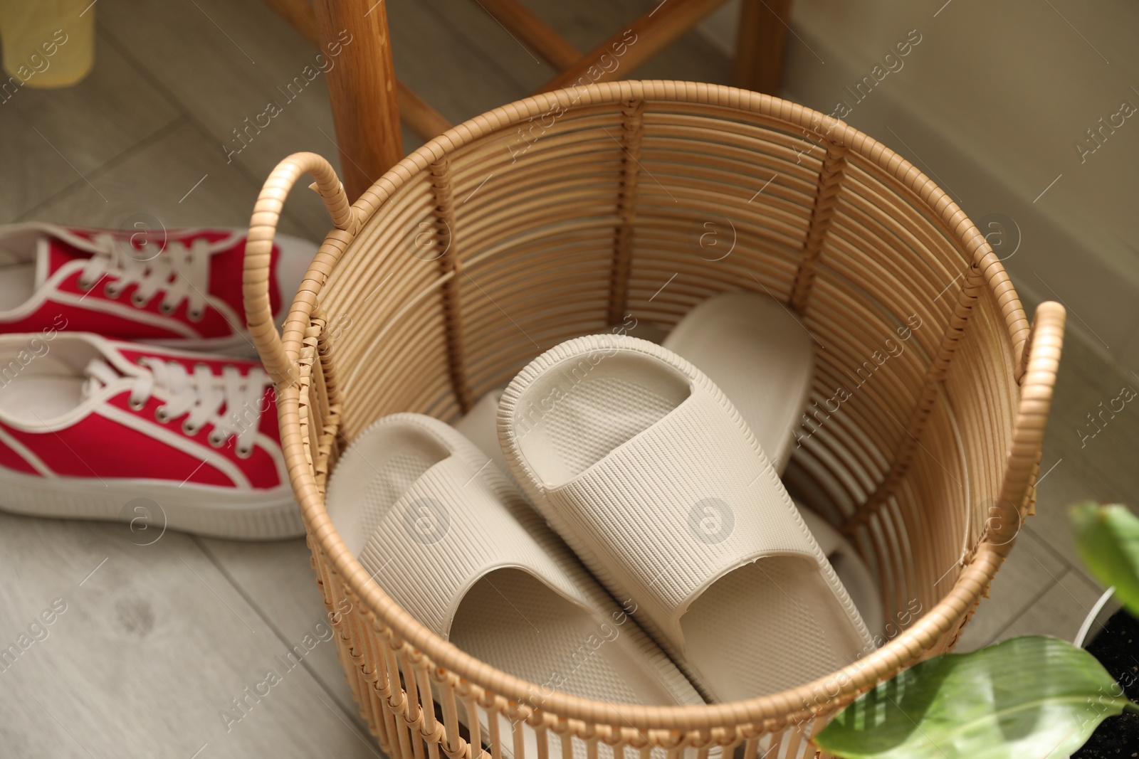 Photo of Basket with slippers for guests and sneakers in entryway at home