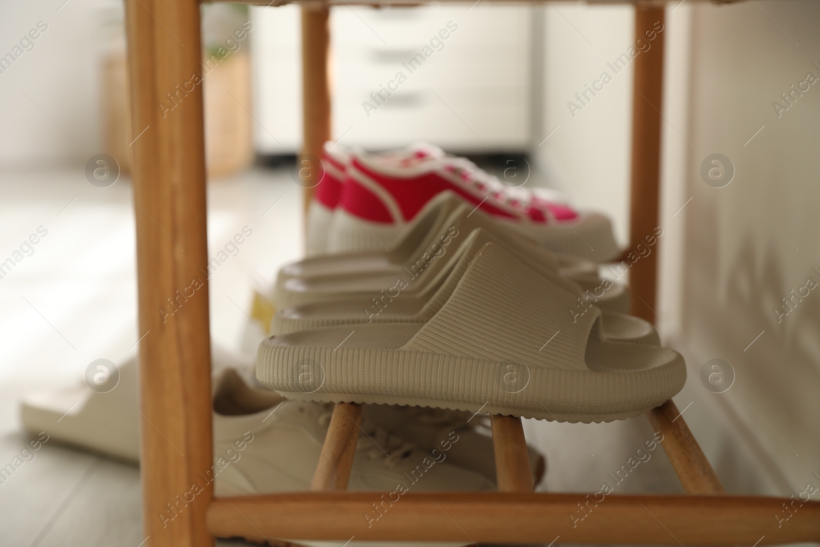 Photo of Pairs of slippers and sneakers on shoe rack at home