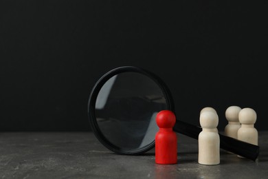 Photo of Red piece among wooden ones and magnifying glass on grey table