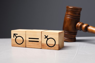 Cube with equals sign between female and male gender symbols near wooden gavel on light table