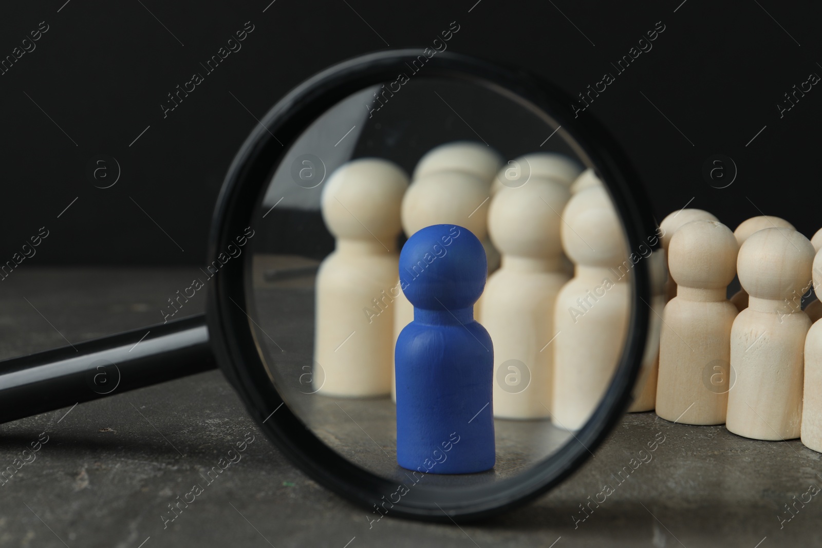 Photo of Blue piece among wooden ones and magnifying glass on grey table, closeup