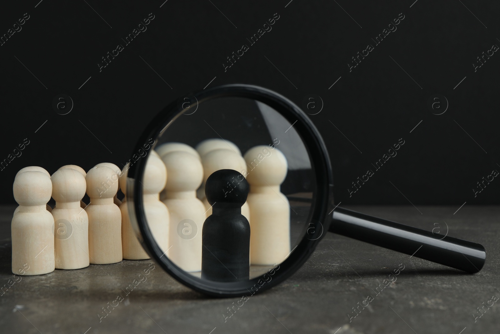 Photo of Black piece among wooden ones and magnifying glass on grey table, closeup