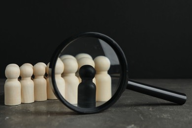 Photo of Black piece among wooden ones and magnifying glass on grey table, closeup