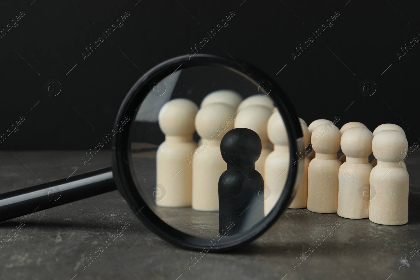 Photo of Black piece among wooden ones and magnifying glass on grey table, closeup