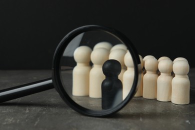 Black piece among wooden ones and magnifying glass on grey table, closeup