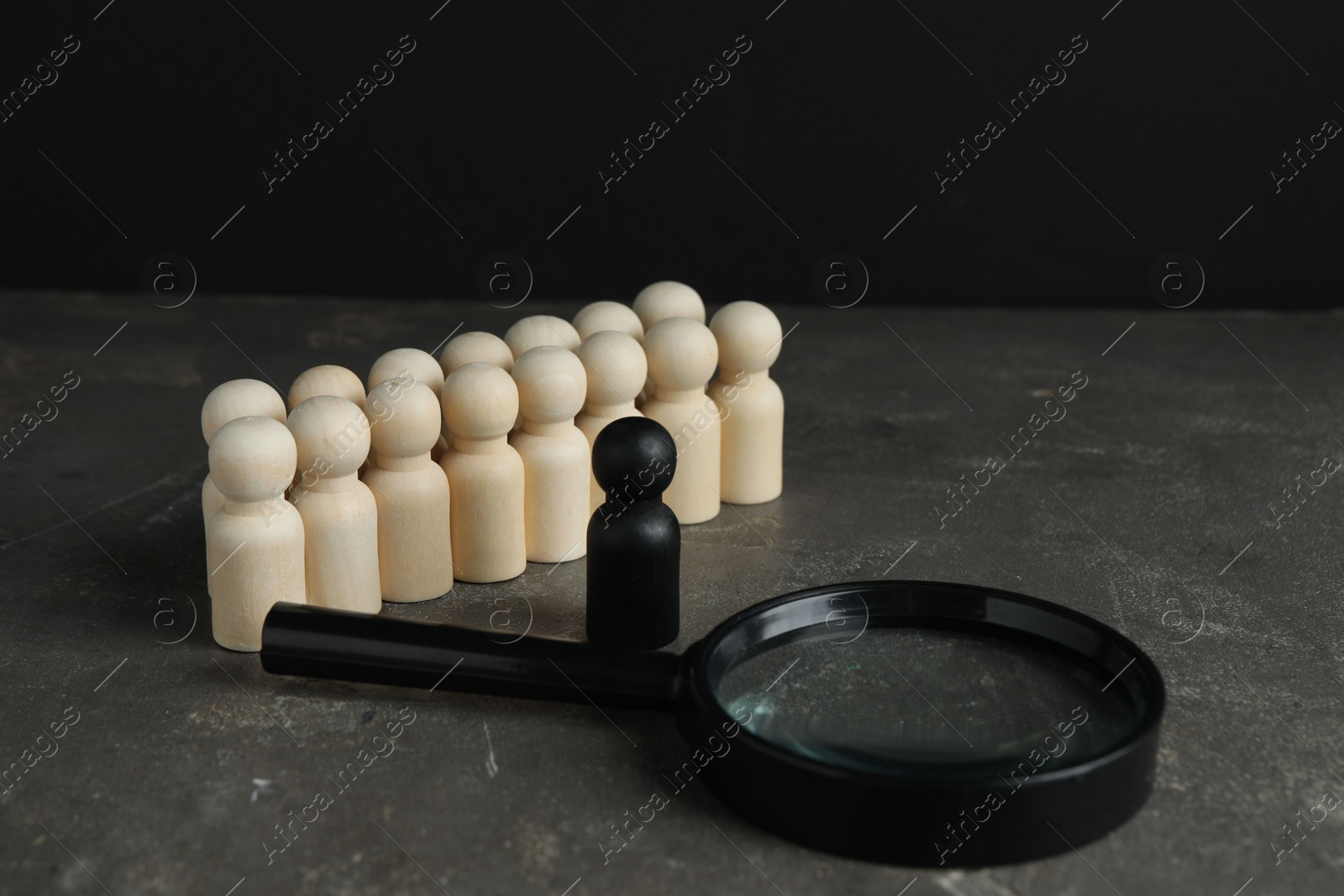 Photo of Black piece among wooden ones and magnifying glass on grey table