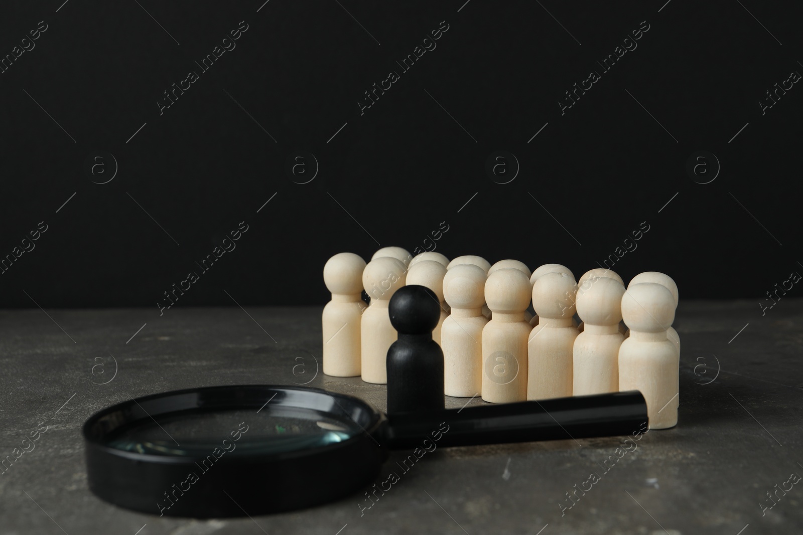 Photo of Black piece among wooden ones and magnifying glass on grey table