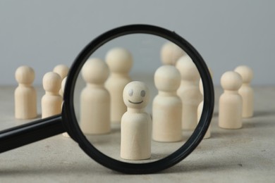 Photo of Magnifying glass showing wooden figure with happy face on grey table, closeup