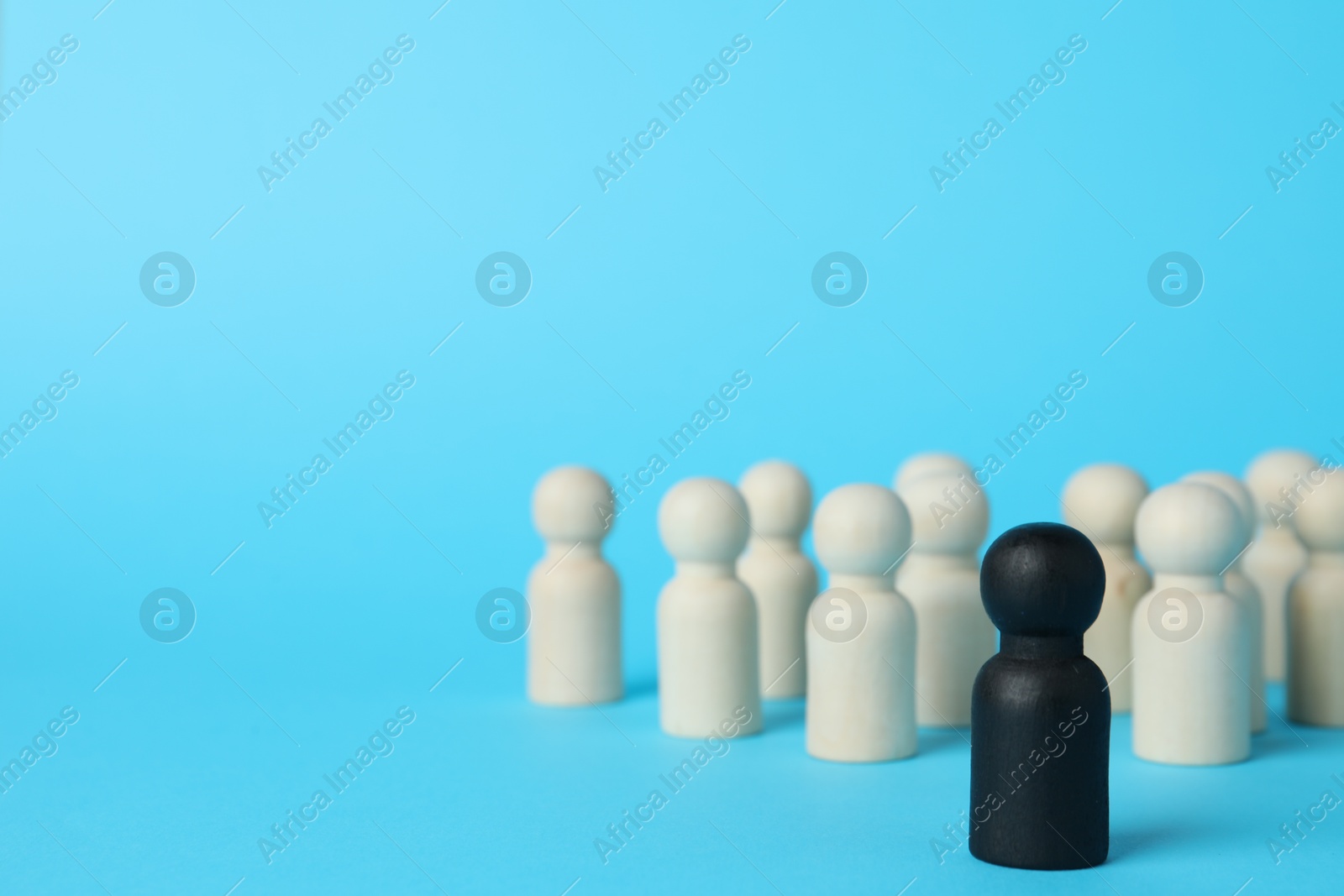 Photo of Black piece among wooden ones on light blue background. Space for text