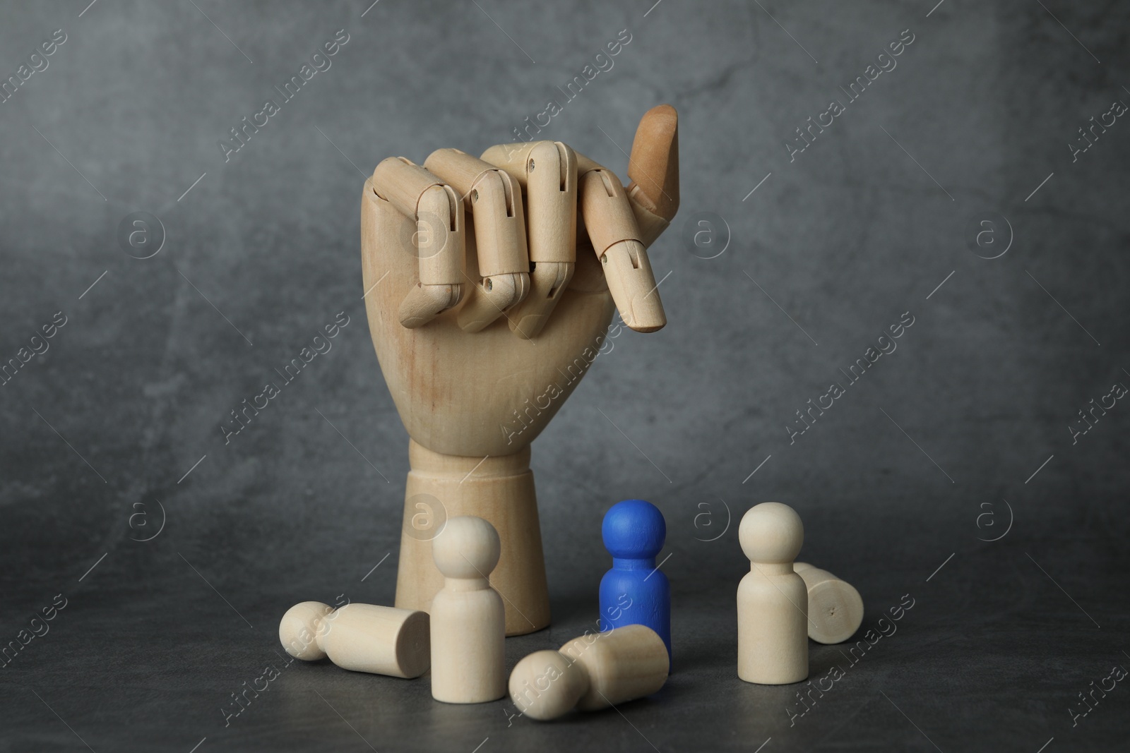 Photo of Blue piece among wooden ones and hand figure on grey table