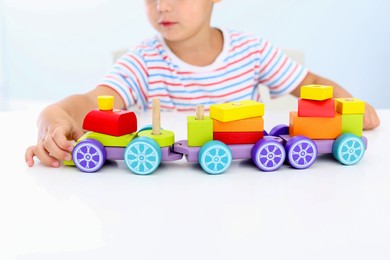 Photo of Little boy playing with toy at white table, closeup