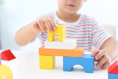 Little boy playing with colorful blocks at white table, closeup. Educational toy