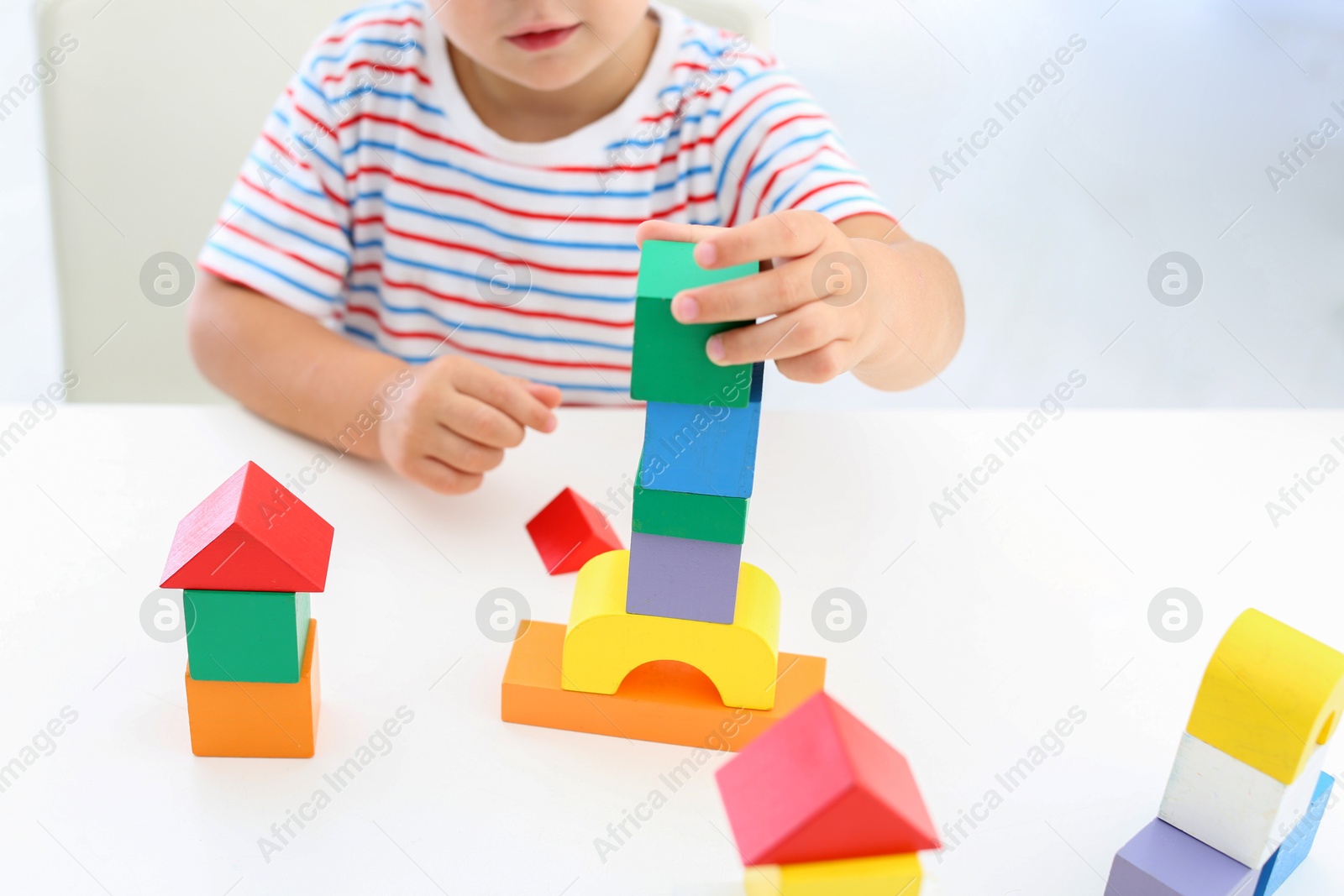 Photo of Little boy playing with colorful blocks at white table, closeup. Educational toy