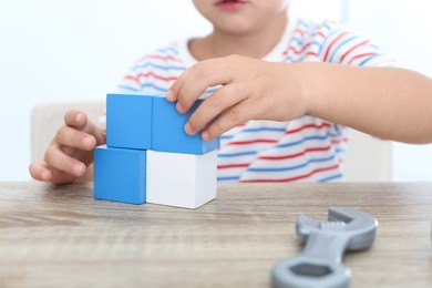 Little boy playing with cubes at wooden table, closeup. Educational toy