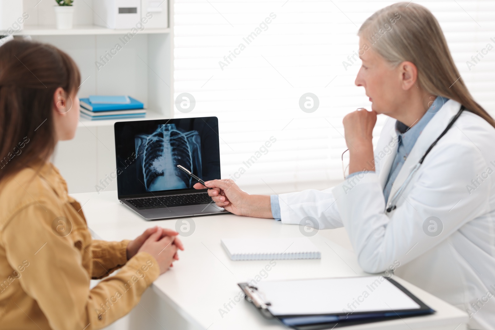 Photo of Lung cancer. Doctor showing chest x-ray on laptop to her patient in clinic