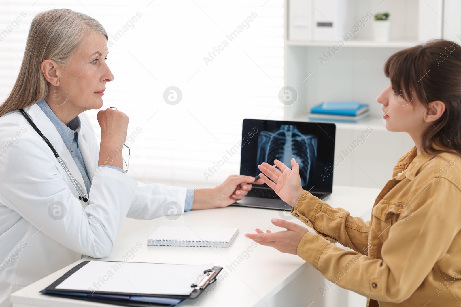 Photo of Lung cancer. Doctor showing chest x-ray on laptop to her patient in clinic