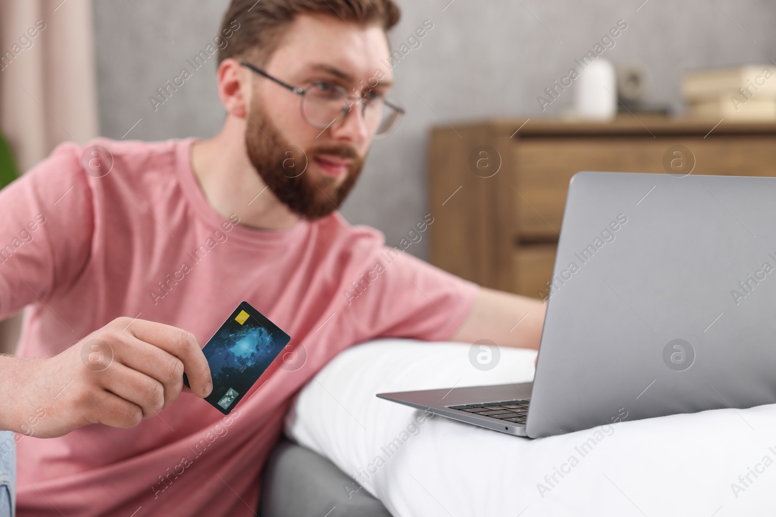 Photo of Online banking. Young man with credit card and laptop paying purchase at home, selective focus