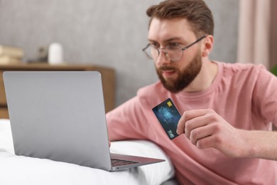 Photo of Online banking. Young man with credit card and laptop paying purchase at home, selective focus