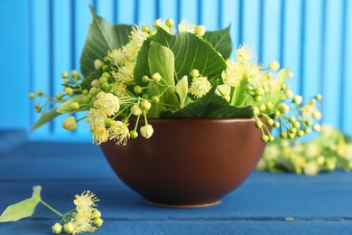 Fresh linden leaves and flowers in bowl on blue wooden table