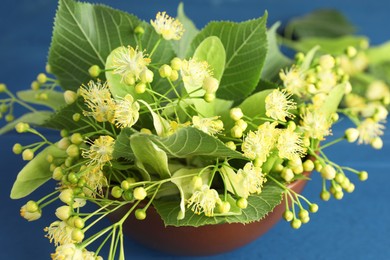 Fresh linden leaves and flowers in bowl on blue wooden table